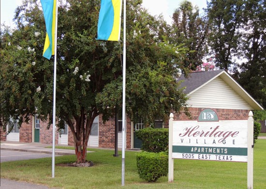 Heritage Village Apartment big front sign with two flags next to it