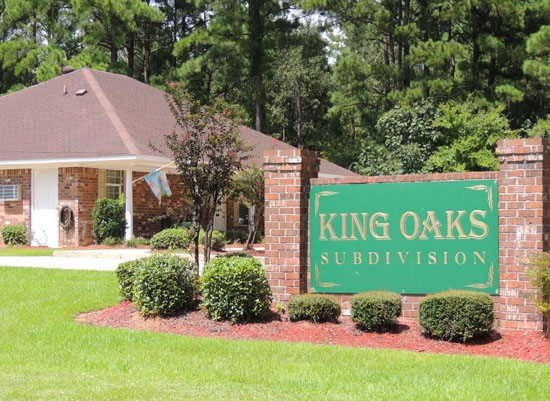 King Oaks Apartments big green front sign with gold letters, surrounded by small bushes, front office in background