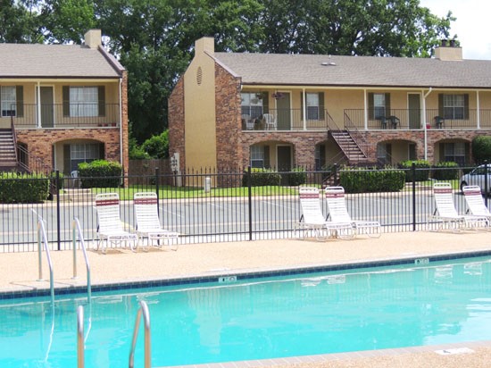 Kingston Village Apartments side view from gate looking at pool, pool side lounge chairs and apartment buildings in background